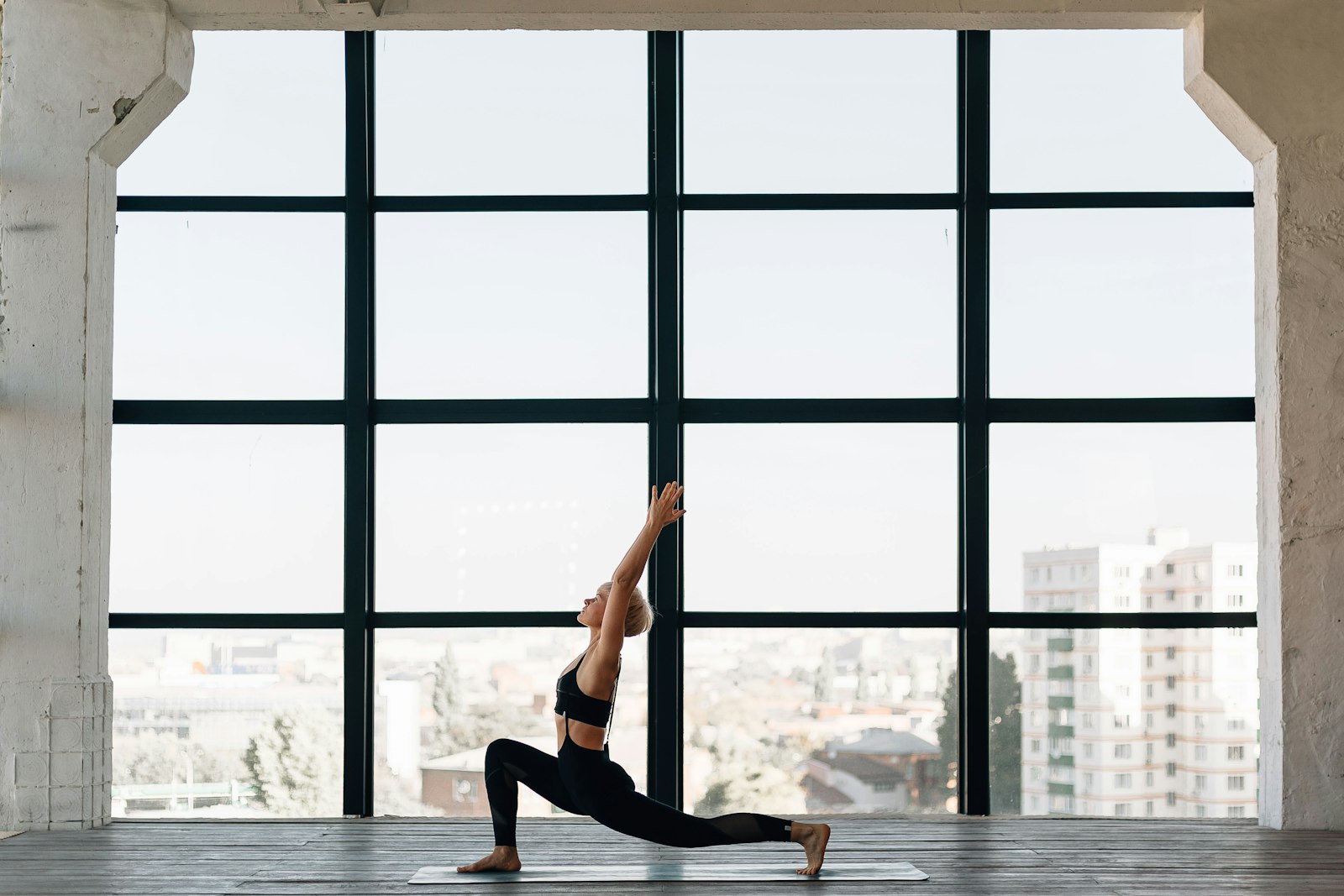 Vrouw in sportkleding doet yoga bij een groot raam