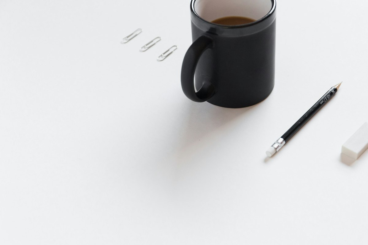 Minimalistische kantoorspullen: mok, potlood, gum en paperclips op een wit bureau