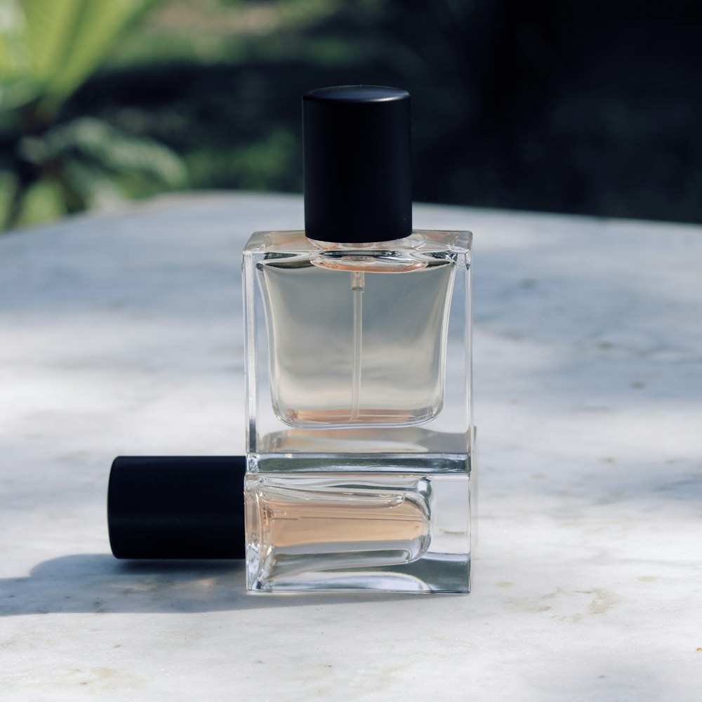 Twee glazen parfumflessen met zwarte dop op een marmeren tafel